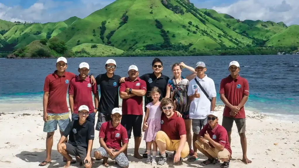 IndonesiaJuara Trip crew and guests posing on a beach below green hills
