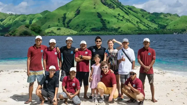 IndonesiaJuara Trip crew and guests posing on a beach below green hills