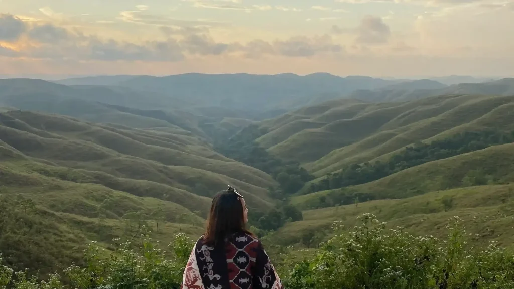Traveller wrapped in an ikat shawl looking over the green valleys of Sumba