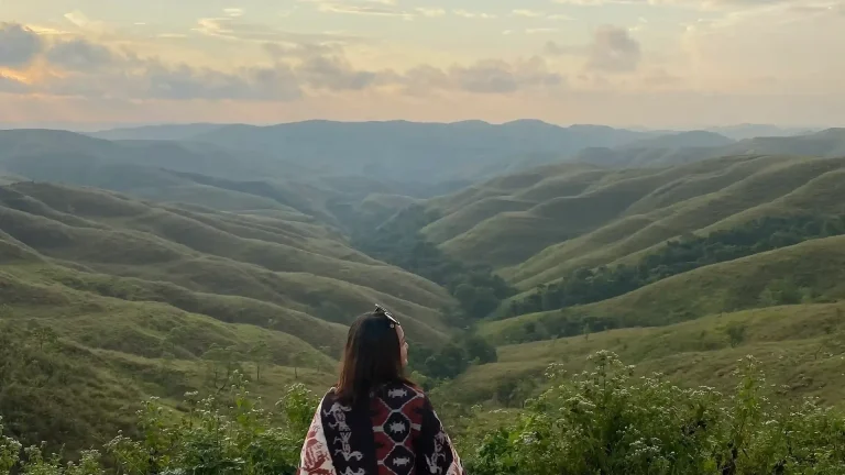 Traveller wrapped in an ikat shawl looking over the green valleys of Sumba