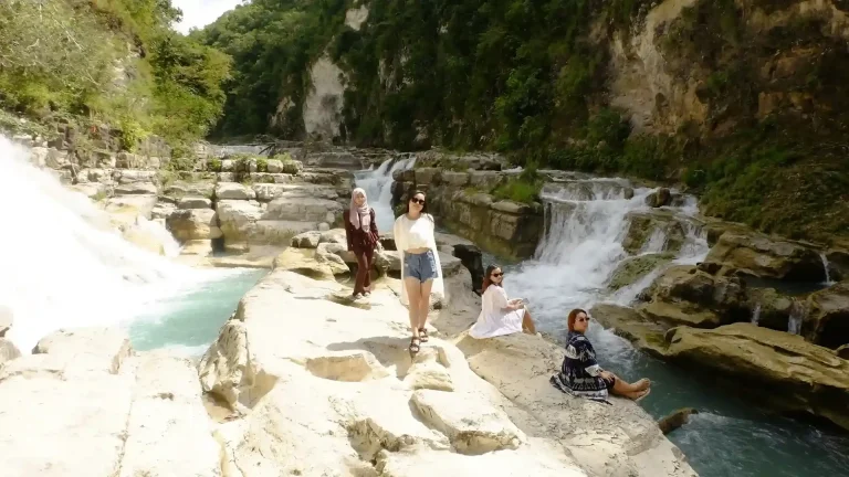Travellers posing for photos on limestone terraces beside a waterfall in Sumba